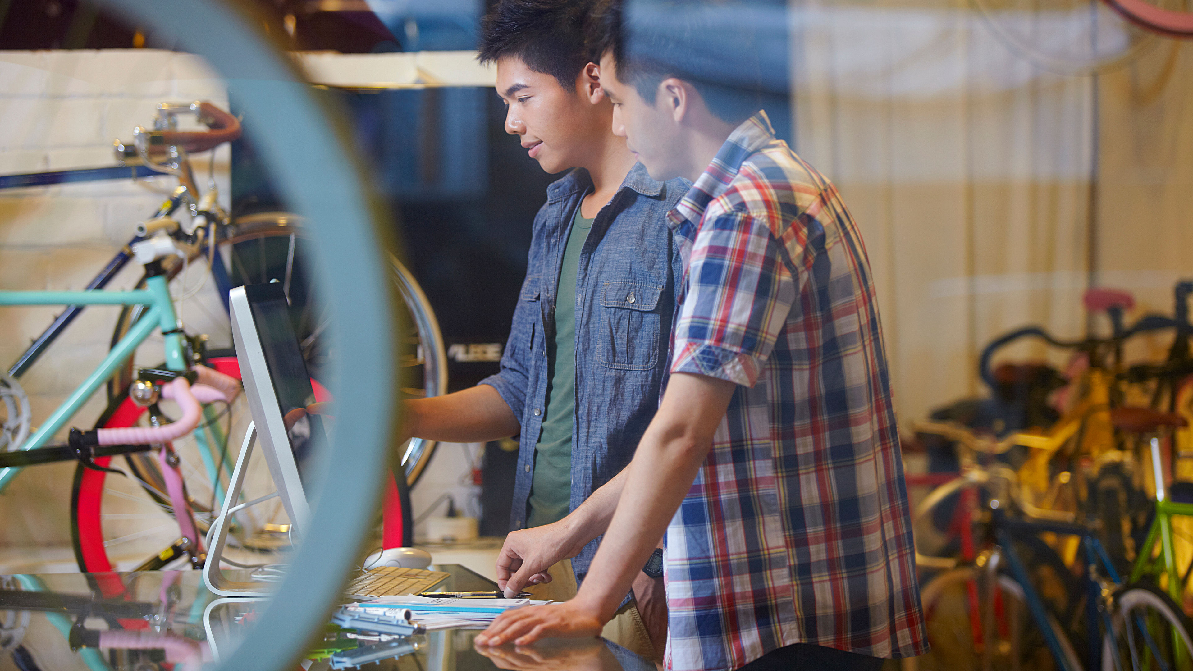 Two young men are looking at something attentively inside a bicycle shop 