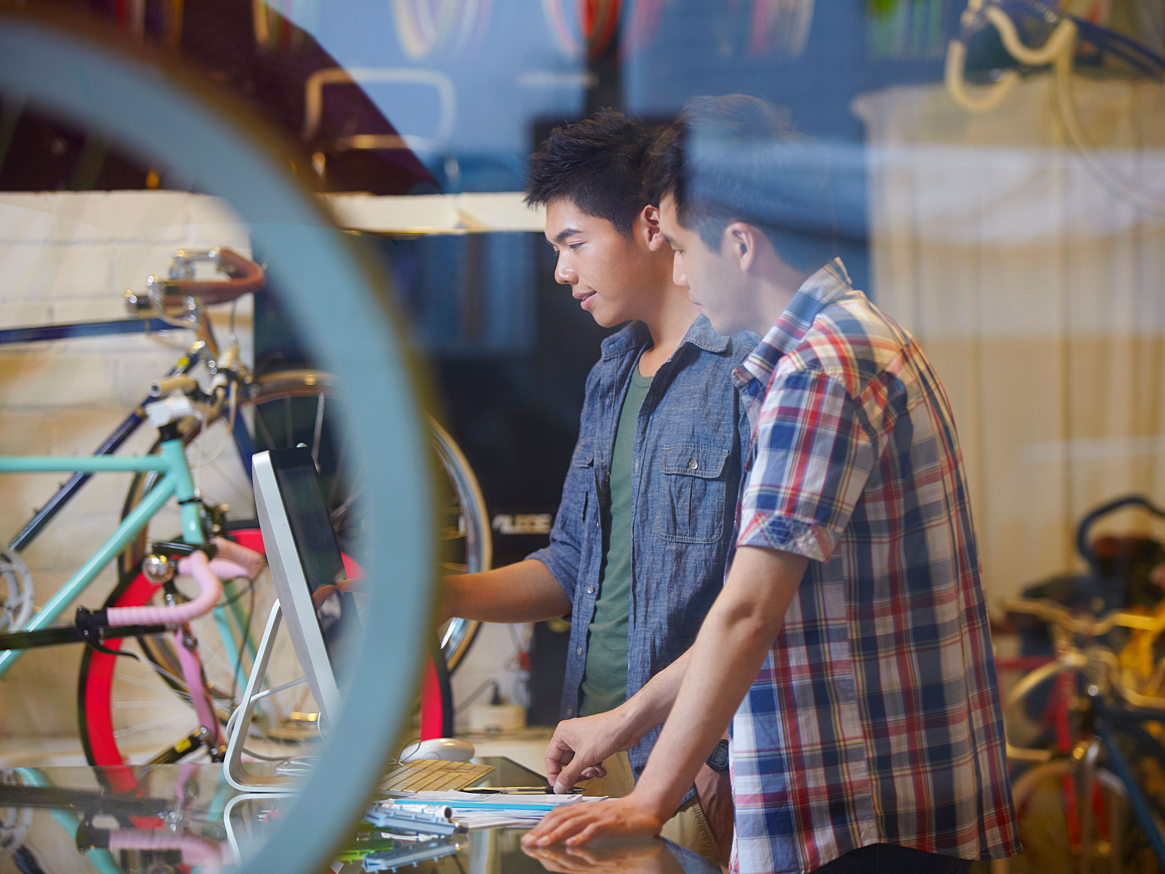 Two young men are looking at something attentively inside a bicycle shop 